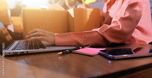 Startup SME small business entrepreneur of freelance Asian woman wearing apron using laptop and box to receive and review orders online to prepare to pack sell to customers, online sme business ideas.
