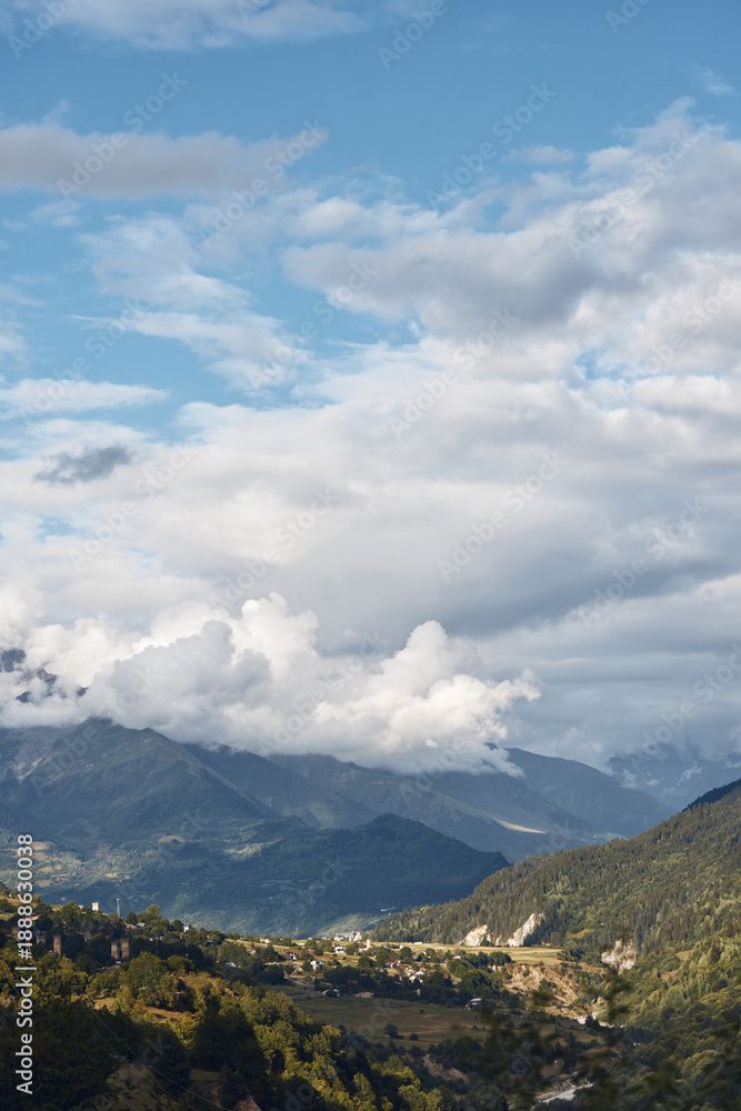 Fototapeta premium Mountain landscape valley and village under dramatic clouds panoramic nature scene with rolling hills and forest