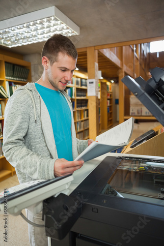 Foto Man standing at library photocopier flipping through stapled booklet near wooden