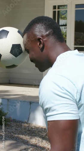 Vertical video: Lifting soccer ball, man in blue tee wearing watch training head control on porch