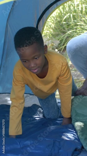 Vertical video: Kid in shirt crawling, testing pad and sitting in tent as adult adjusting green bag