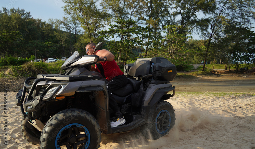 Fototapeta premium A man engages in extreme ATV riding on sand beach early in the morning