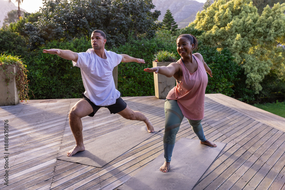Obraz premium Diverse couple practicing yoga in sportswear on open-air deck with yoga mats, potted plants