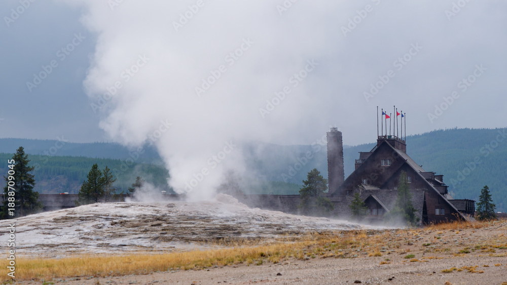 Fototapeta premium View of the Old Faithful Inn and steaming geyser eruption in Yellowstone National Park, Wyoming, USA