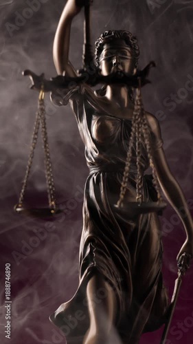 Dramatic white smoke flowing around the bronze scales and blindfolded face of a Lady Justice statue set against a deep purple background.