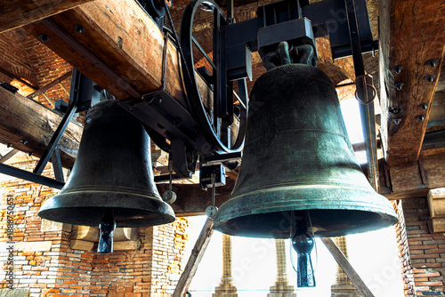Ancient church bells hanging inside the stone bell tower of the Basilica of San Frediano in Lucca, Italy, showcasing medieval architecture and religious heritage.