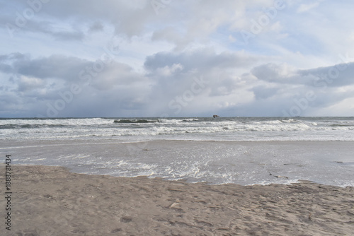 Dramatic stormy sky over an empty sandy beach with waves and dark clouds. Moody seascape landscape with strong wind, cold atmosphere and vast open space. Minimalist coastal scenery, solitude and natur