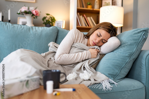 Exhausted sick young woman sleeping on sofa at home covered with blanket suffering from fatigue fever or flu recovery with medicine and tea on table nearby healthcare and resting concept