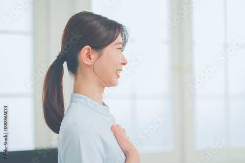 明るく清潔感のあるクリニックでにこやかに笑う20代女性看護師