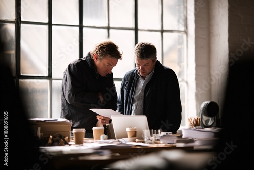 Two men collaborating over documents and laptop in a modern office space