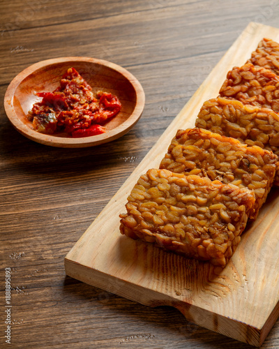 Tableau sur toile Fried tempeh slices arranged on wooden board with sambal tomat in small bowl, tr