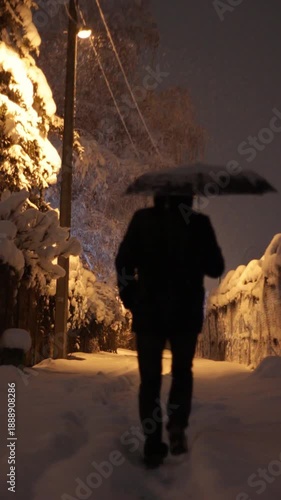 Man with umbrella walking in a snowy alley at night.