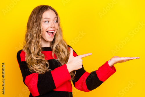 Excited young woman in casual striped sweater pointing and smiling with cheerful expression on vibrant yellow background