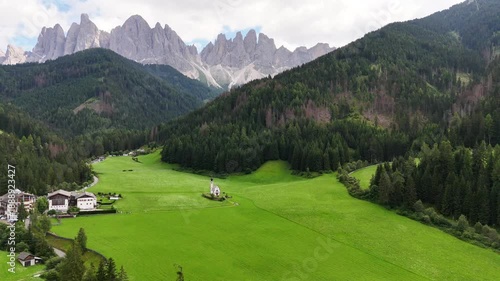 Drone flight, bird view, toward church of San Giovanni in Ranui near beautiful village of St Magdalena, Val di Funes, South Tyrol. Wonderful valley with impressive Dolomites, sharp peaks. travel desti