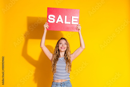 Young woman holding a sale sign on yellow background showcasing excitement for shopping and promotions