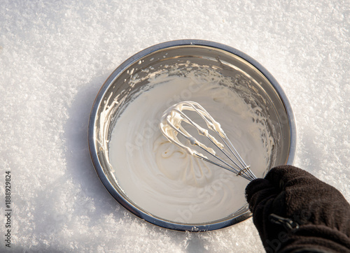 Canvas Print Person hand whisks whipping cream, making ice cream, hand-churning ice cream in metal bowl in snow outdoors in winter