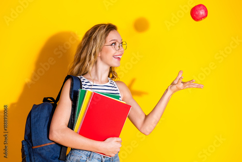 Fotografie Cheerful young woman with blonde hair holding book and tossing an apple against