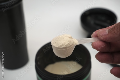 Close-up of a hand holding a scoop of creatine monohydrate powder taken from an open supplement container