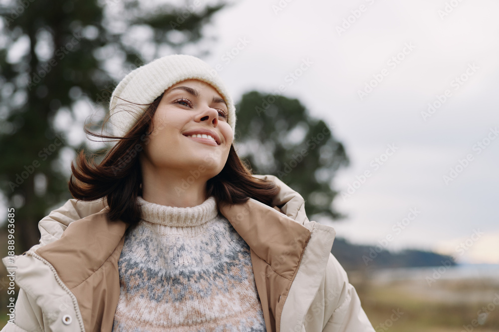 Fototapeta premium Woman outdoors in a cozy beanie and jacket, smiling with the breeze in a natural landscape, capturing warmth, happiness and carefree mood in fresh air.