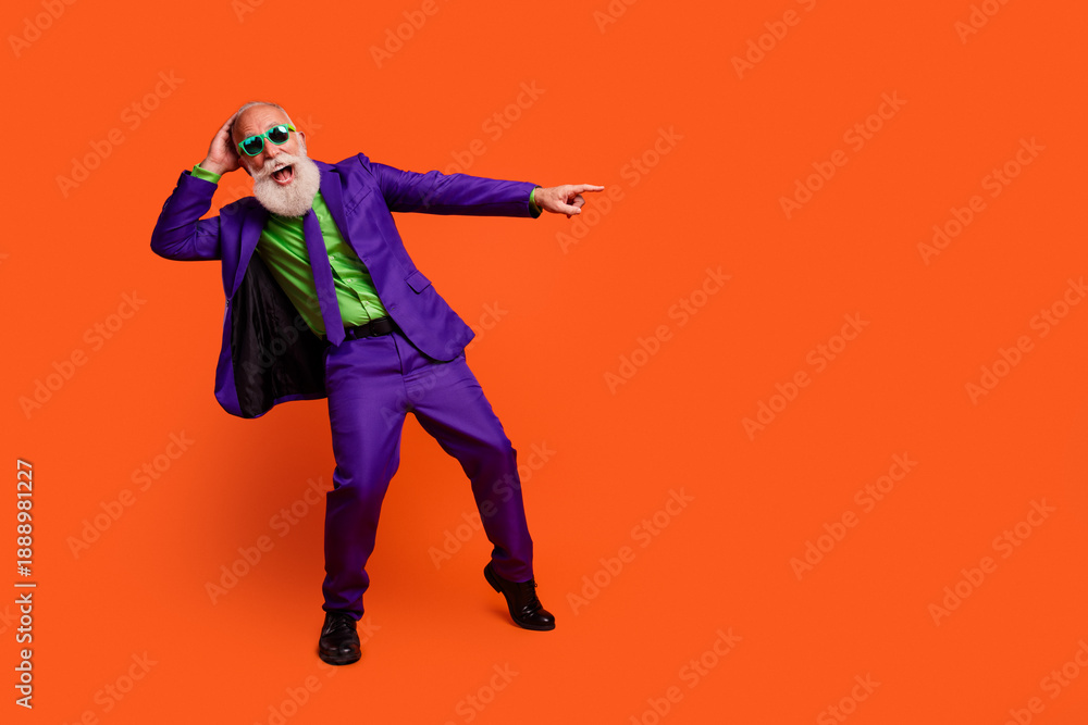 Obraz premium Cheerful retired man in a purple suit dances playfully against orange background