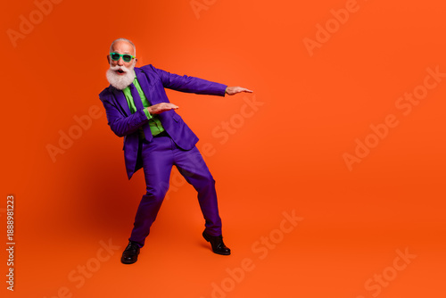 Energetic elderly man in purple suit dances in bright orange studio with green shirt creating joyful retro style