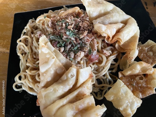 Close-up of Indonesian Fried Noodles Topped with Minced Meat and Crispy Fried Wontons on a Black Plate