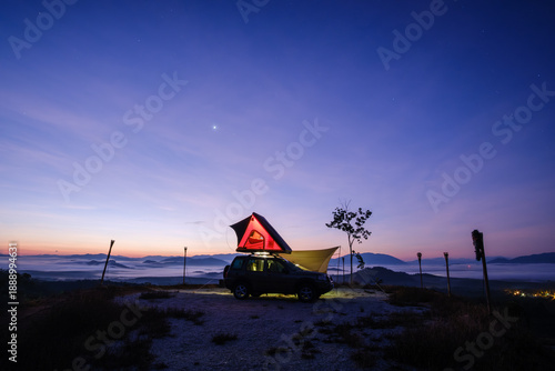 Side view silhouette of an illuminated off road vehicle with a tent on top parked on a mountain at sunset, Yan, Kedah, Malaysia