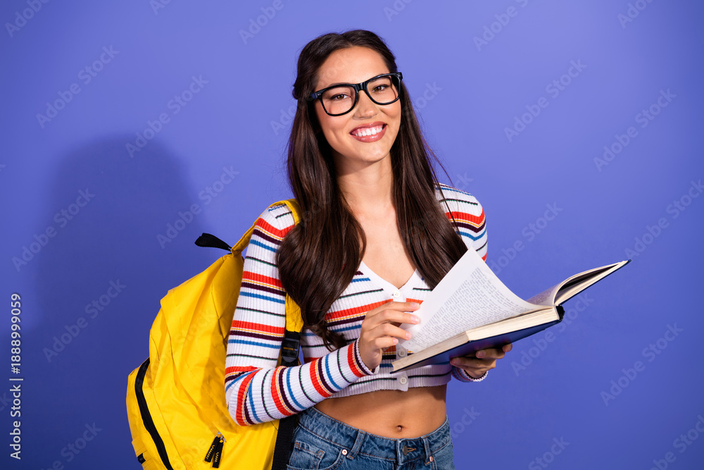 Fototapeta premium Young woman student reading book with yellow backpack smiling against blue background