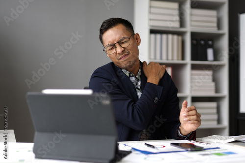 Foto Stressed businessman suffering from neck pain and shoulder pain while working on laptop in office