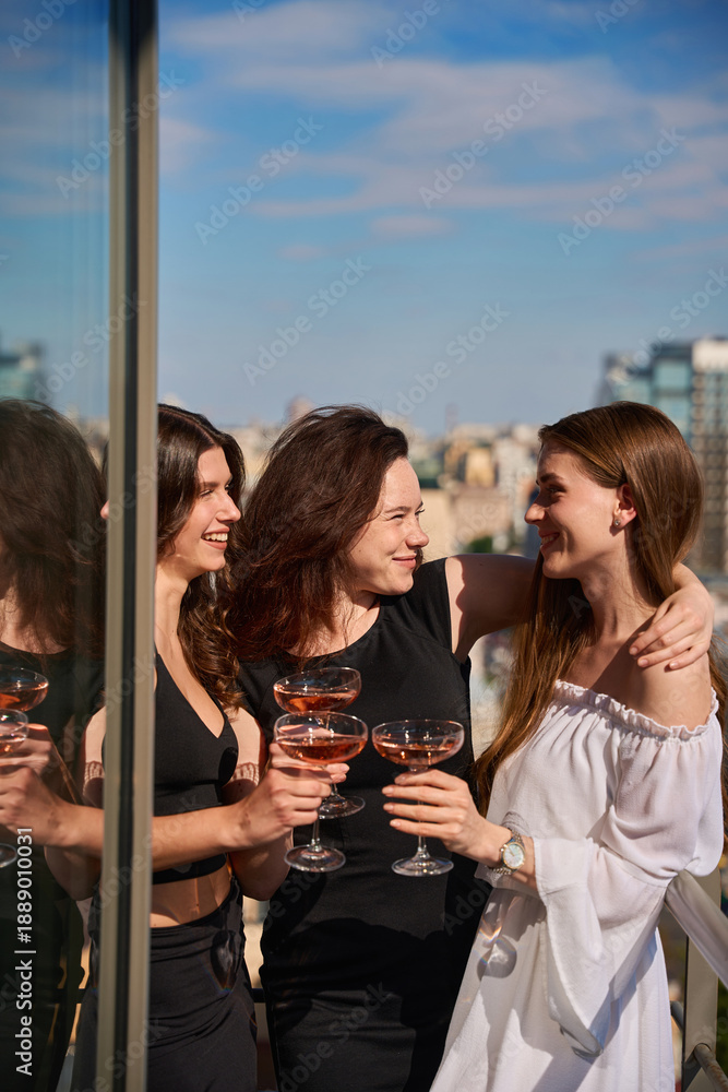 Fototapeta premium Happy girlfriends making a toast with glasses of champagne on terrace outdoors