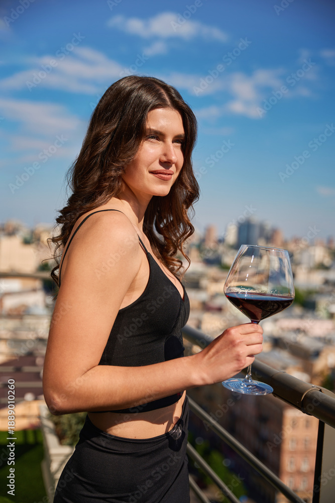 Fototapeta premium Pretty young woman posing with red wine enjoying view on the terrace