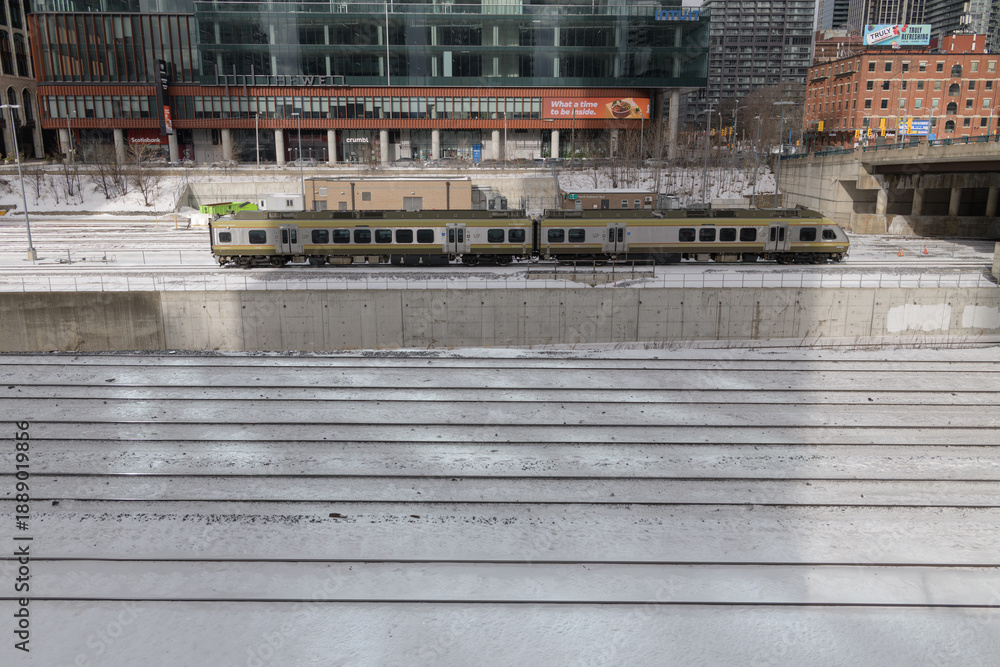 Obraz premium Union Pearson Express zooming by on the Union Station Rail Corridor with view of The Well complex, viewed from Iceboat Terrace, Toronto