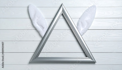 A silver triangle frame sits on white wooden planks, with white rabbit ears peeking out, creating a whimsical spring or Easter design