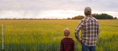 Farmer and his son in front of a sunset agricultural landscape. Man and a boy in a countryside field. Fatherhood, country life, farming and country lifestyle concept.