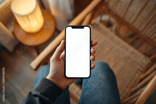 A Person is checking a white screen mobile phone and a laptop is in the background