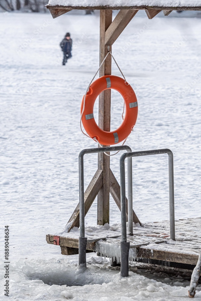 Fototapeta premium Hole in a frozen lake with wooden pier and lifesaver covered in snow ready for cold therapy, ice bathing. Wim Hof Method, cold therapy, breathing techniques, yoga and meditation