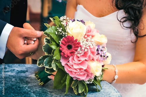 Wedding bouquet in the hands of the bride and groom: pink roses, gerberas and delicate white flowers