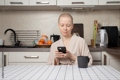 young woman with short regrown hair after chemotherapy sits in a cozy kitchen,