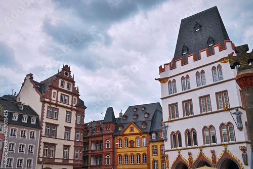 A colorful medieval European town square with historic buildings against a cloudy sky