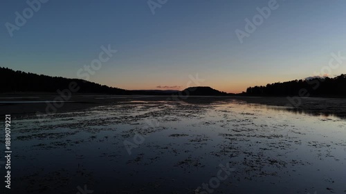 Aerial view of a calm lake at twilight with sunset reflections on the water surface and forest silhouette background