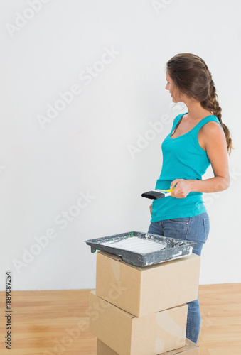 Paintbrush is resting in tray on stacked cardboard boxes on hardwood floor, wall is being primed