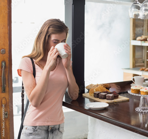 White ceramic cup steaming while sitting on wooden counter near window, pastries displayed nearby