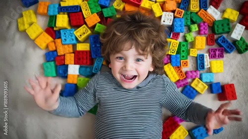 Young boy smiling widely, lying on a vibrant background of construction toy bricks