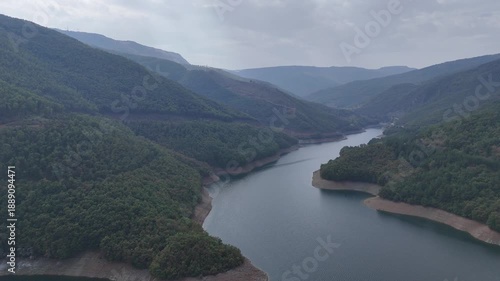 Aerial panoramic view of a winding river flowing through lush green mountains under an overcast sky, scenic valley landscape, tranquil nature background.