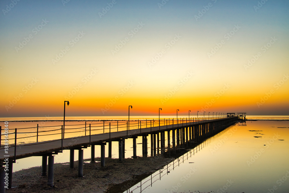 Obraz premium A breathtaking sunset over the Red Sea in Egypt, with a long wooden pier stretching across calm, reflective water.