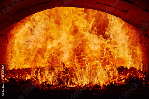 Inside view of an industrial furnace with roaring orange flames and glowing coal.