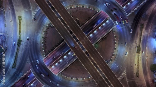 Drone view of nighttime car lanes, highway, and intersections in the city, city road, car lanes, expressway between buildings, traffic flow on city road, expressway and highway, traffic junction car