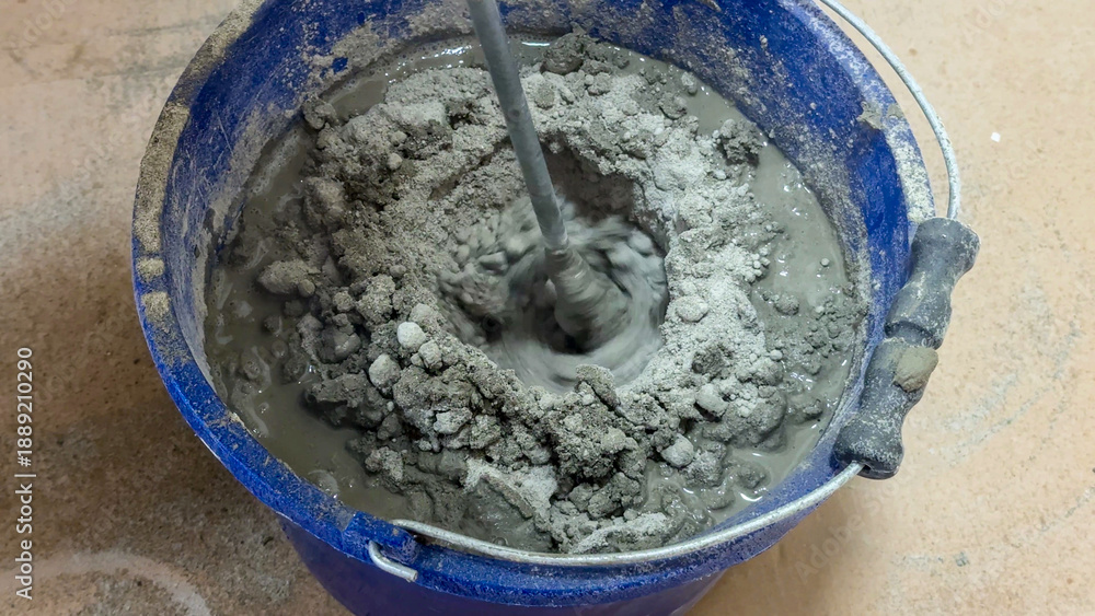 Naklejka premium Mixing concrete in a cerulean bucket, industrial alchemy, building dreams recipe, nod to Worker's Day festivities