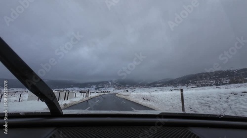 Car driving on a wet road towards a ski resort in Les Angles under a cloudy sky in winter