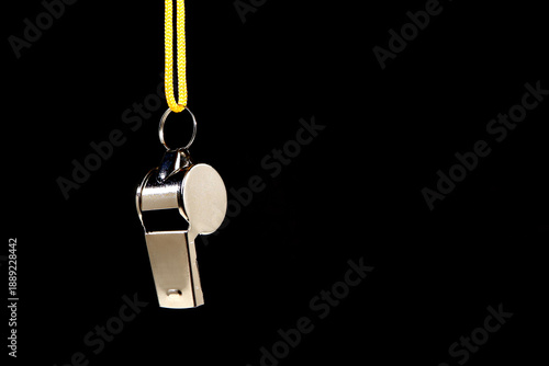 Photography Silver metal referee whistle with bright yellow lanyard hanging isolated against